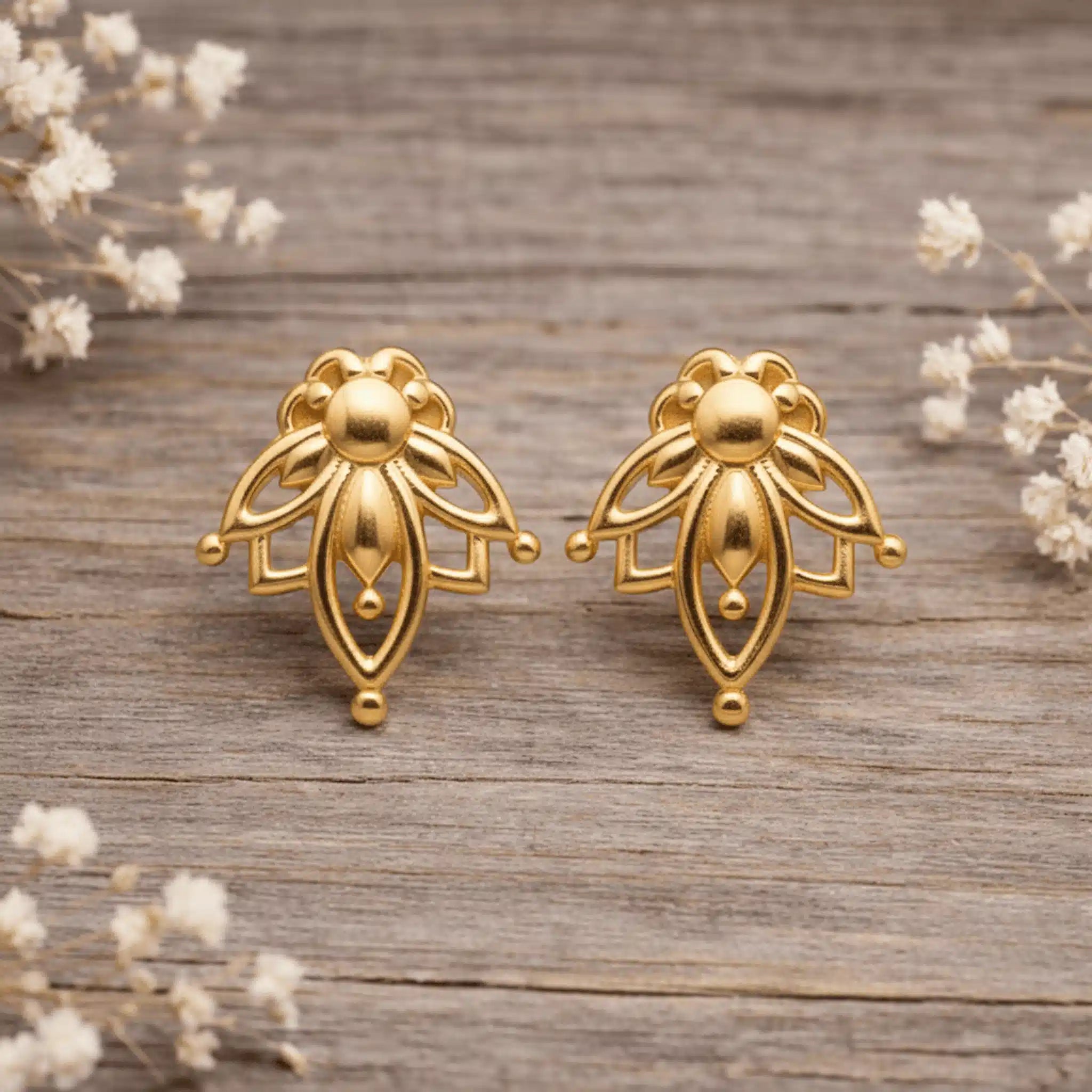 Gold lotus stud earrings on a wooden surface with small white flowers
