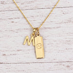 Gold Initial M Pendant and Cancer Zodiac Pendant Necklace on a fine gold chain against a light wooden background