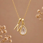 Gold initial M necklace with an April clear quartz teardrop on brown with dried flowers