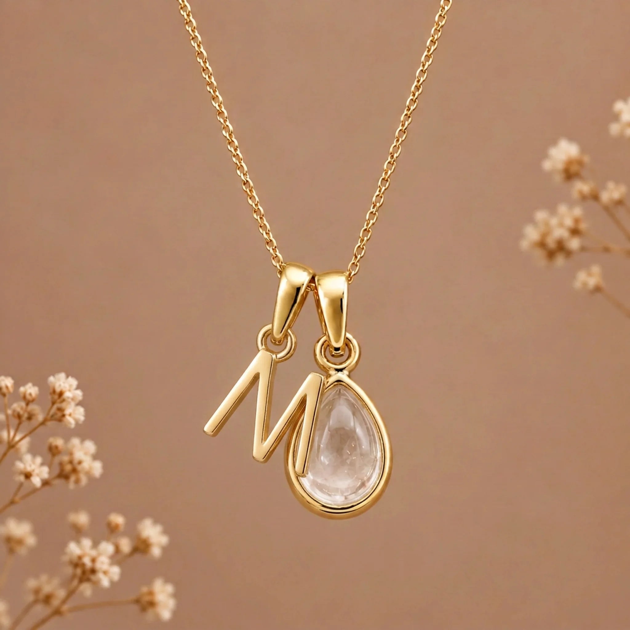 Gold initial M necklace with an April clear quartz teardrop on brown with dried flowers