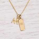 gold M initial and aquarius zodiac necklace on fine gold chain against a light wooden background