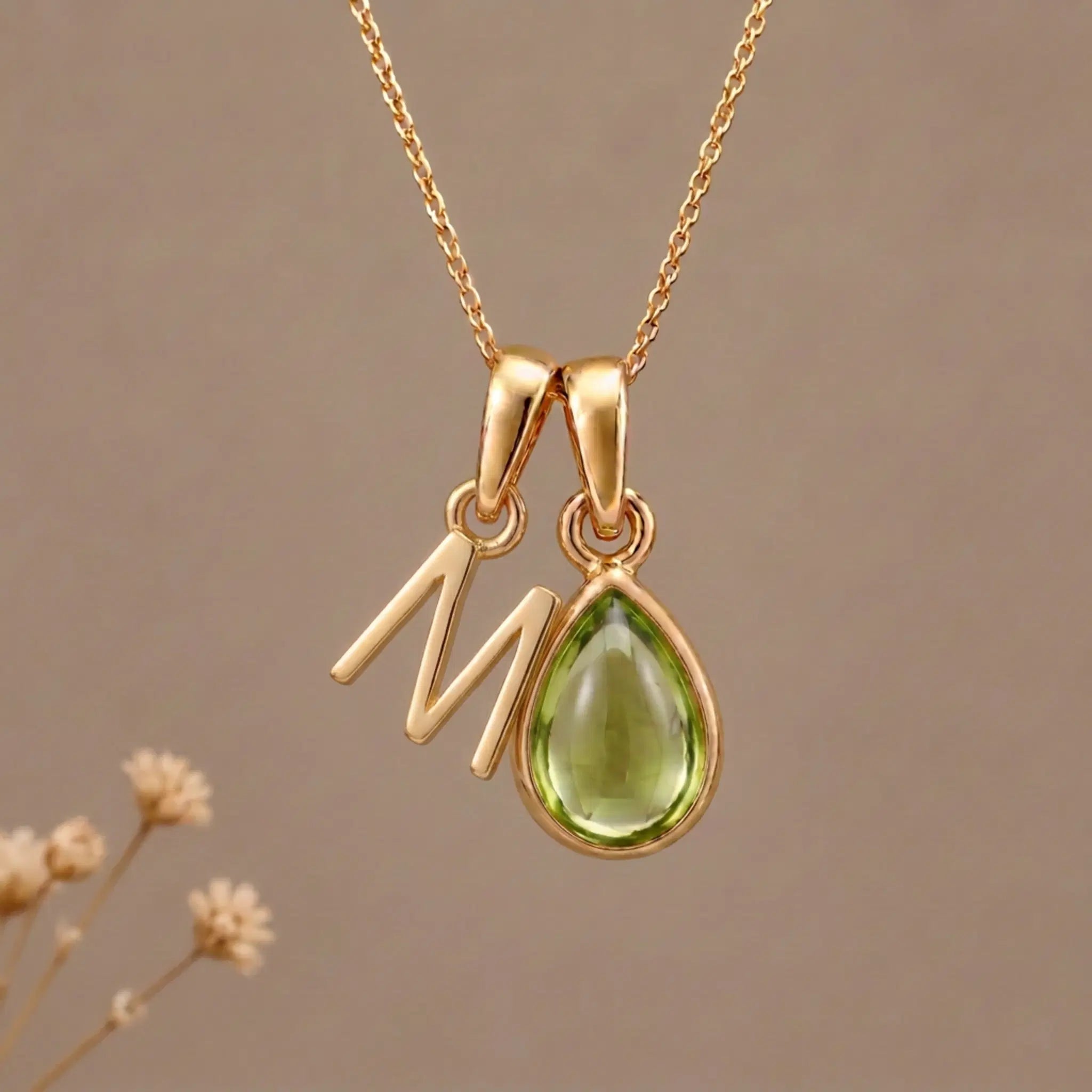 Gold Initial M Pendant and August birthstone Natural Peridot Necklace against a warm background