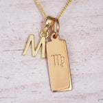 Gold M Initial and Virgo Necklace on a fine gold chain against a light wooden background