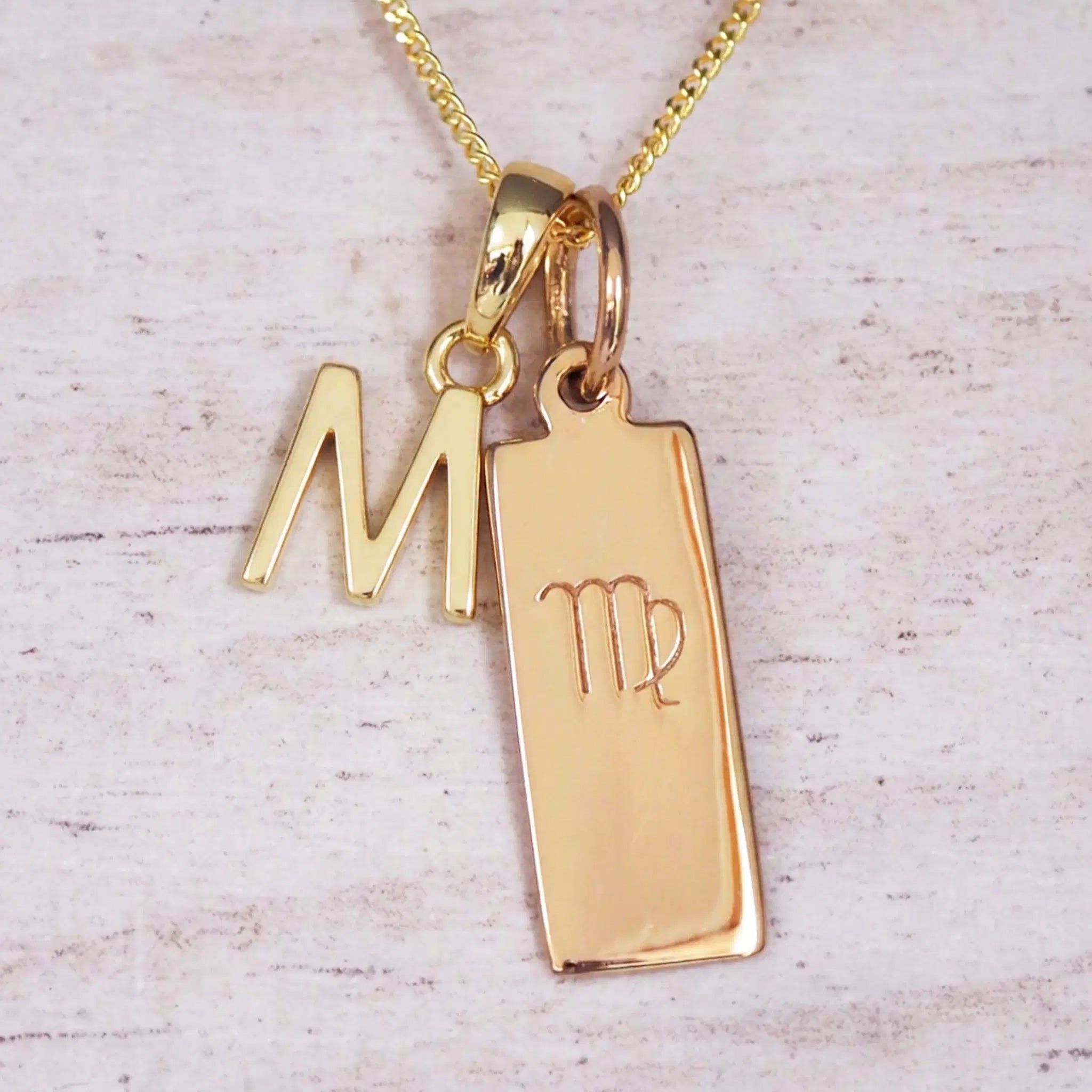 Gold M Initial and Virgo Necklace on a fine gold chain against a light wooden background
