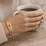Hands holding a coffee cup wearing a gold cuff 