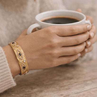 Hands holding a coffee cup wearing a gold cuff 