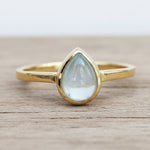 Gold ring with a teardrop-shaped light blue aquamarine gemstone on a wooden surface