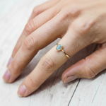 Gold ring with a tear drop shaped aquamarine gemstone on a finger against a light background