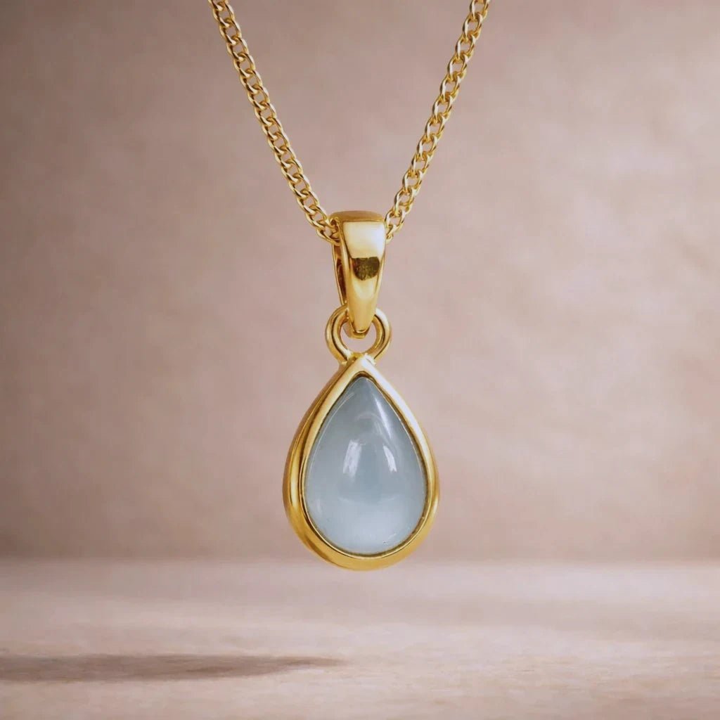 Gold necklace with a teardrop-shaped natural aquamarine gemstone pendant on a beige background