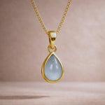 Gold necklace with a teardrop-shaped natural aquamarine gemstone pendant on a beige background