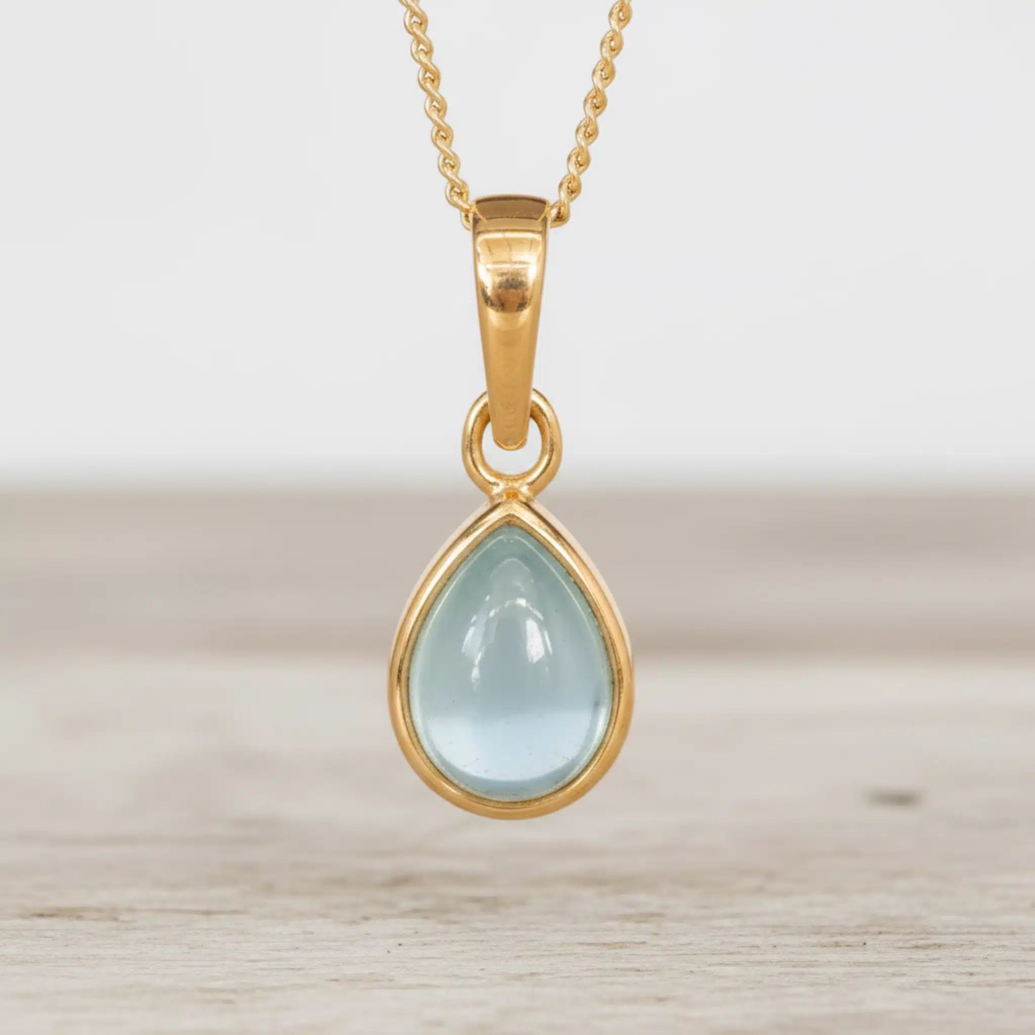 Gold March Birthstone Necklace with a light blue teardrop-shaped natural aquamarine gemstone on a light surface