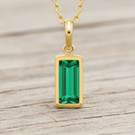 Gold necklace with a green gemstone pendant on a white background
