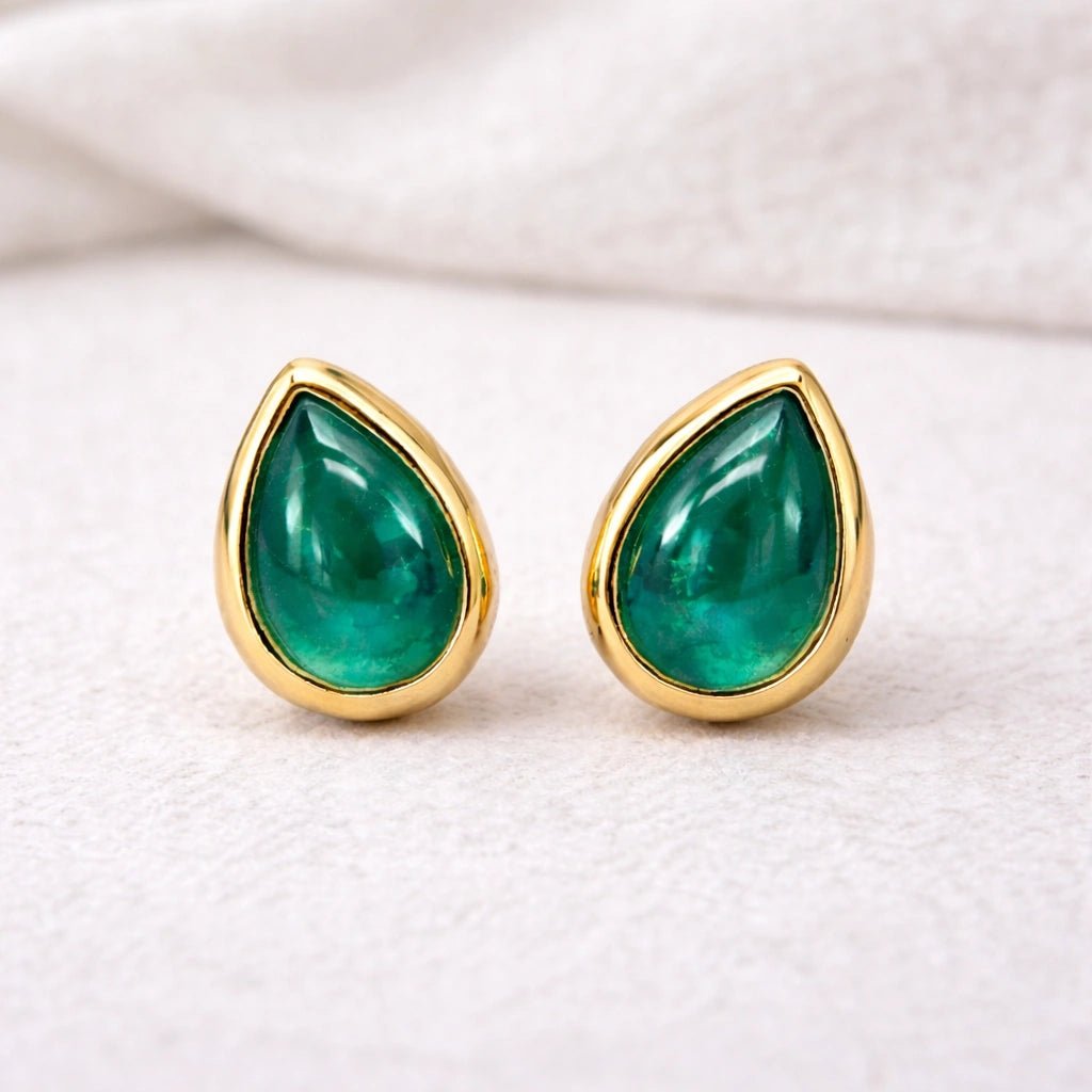 Gold stud earrings with may birthstone green natural emerald teardrop stones on a light background