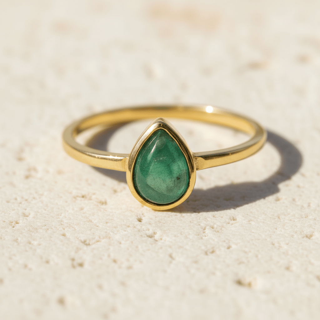 Gold ring with a green natural emerald teardrop-shaped gemstone on a beige background