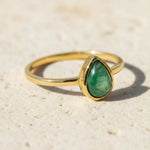 Gold ring with a may birthstone green emerald gemstone on a wooden surface