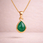 Gold necklace with a green teardrop natural emerald gemstone pendant on a light pink background