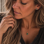 model wearing a gold may birthstone jewellery set of dainty natural emerald pendant necklace and matching stud emerald earrings