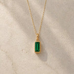 Gold fine chain necklace with a rectangle faceted bezel set may cubic zirconia pendant on a light stone background.