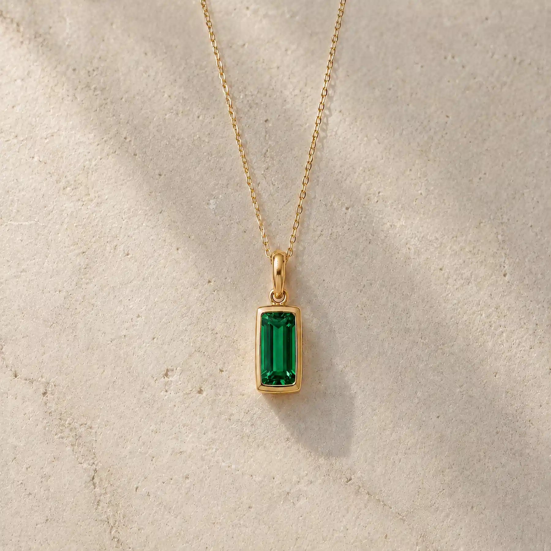 Gold fine chain necklace with a rectangle faceted bezel set may cubic zirconia pendant on a light stone background.