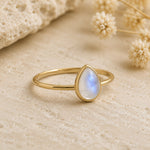 side shot of a gold vermeil teardrop natural moonstone ring on a light stone surface