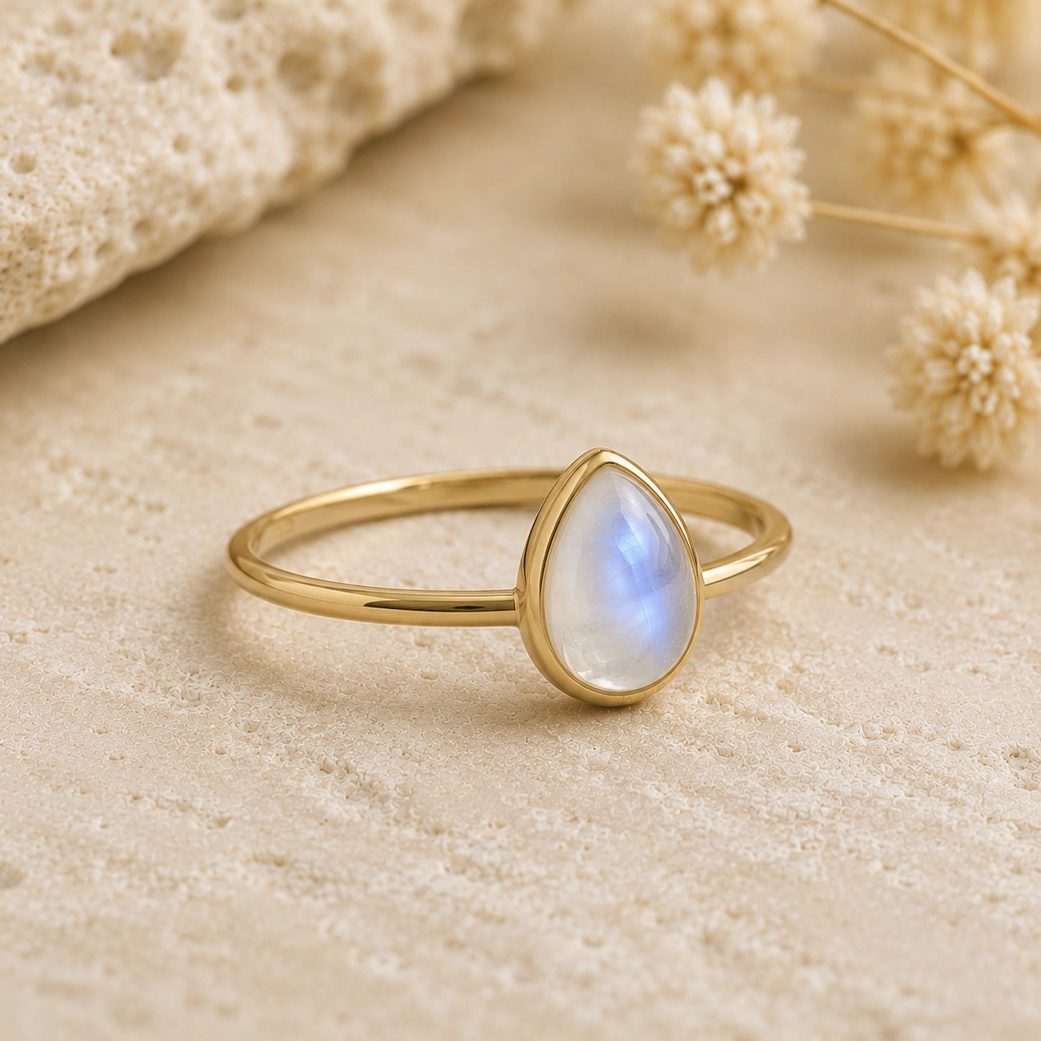 side shot of a gold vermeil teardrop natural moonstone ring on a light stone surface