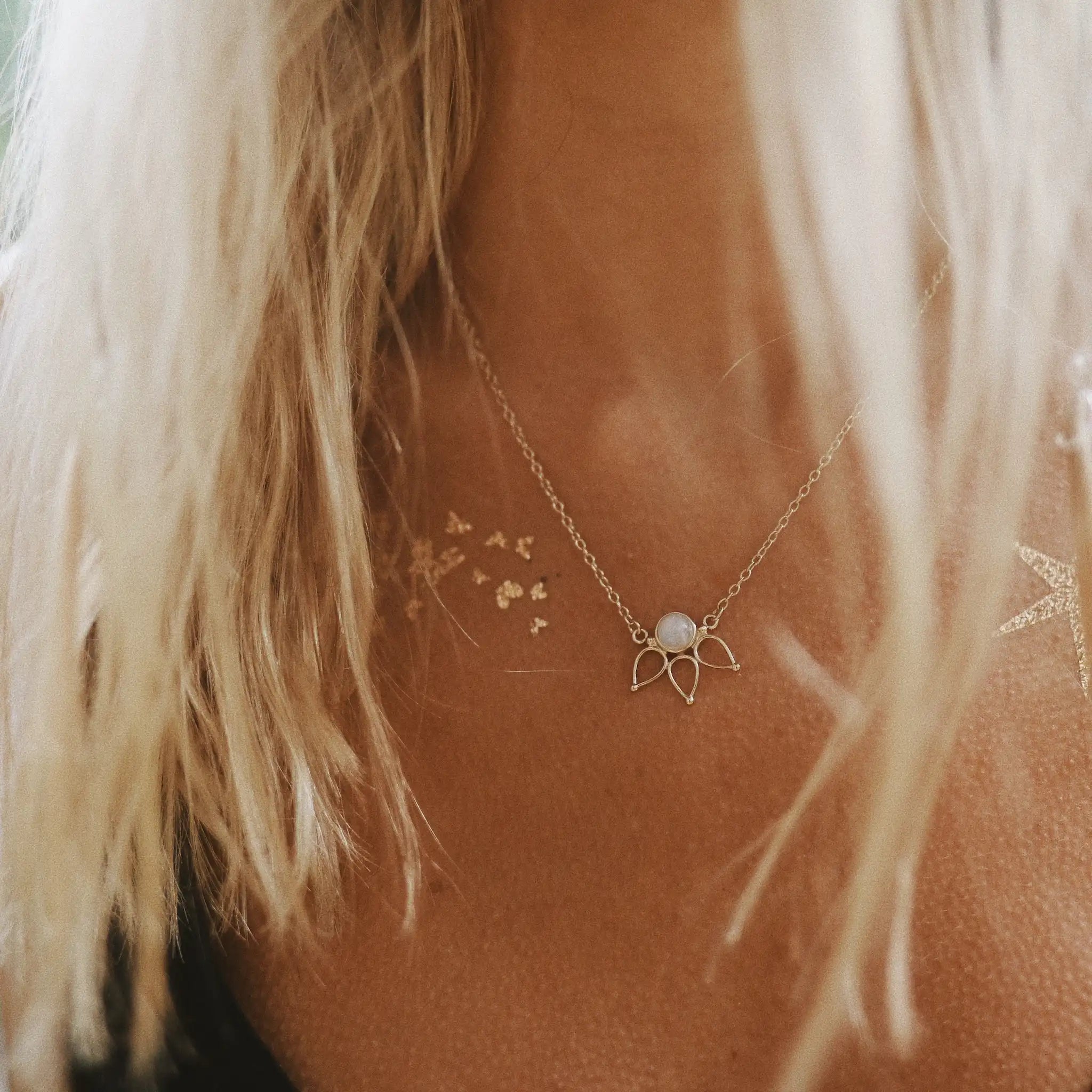 A close-up lifestyle shot of a woman wearing a delicate gold chain necklace with a small natural moonstone on a lotus style pendant.