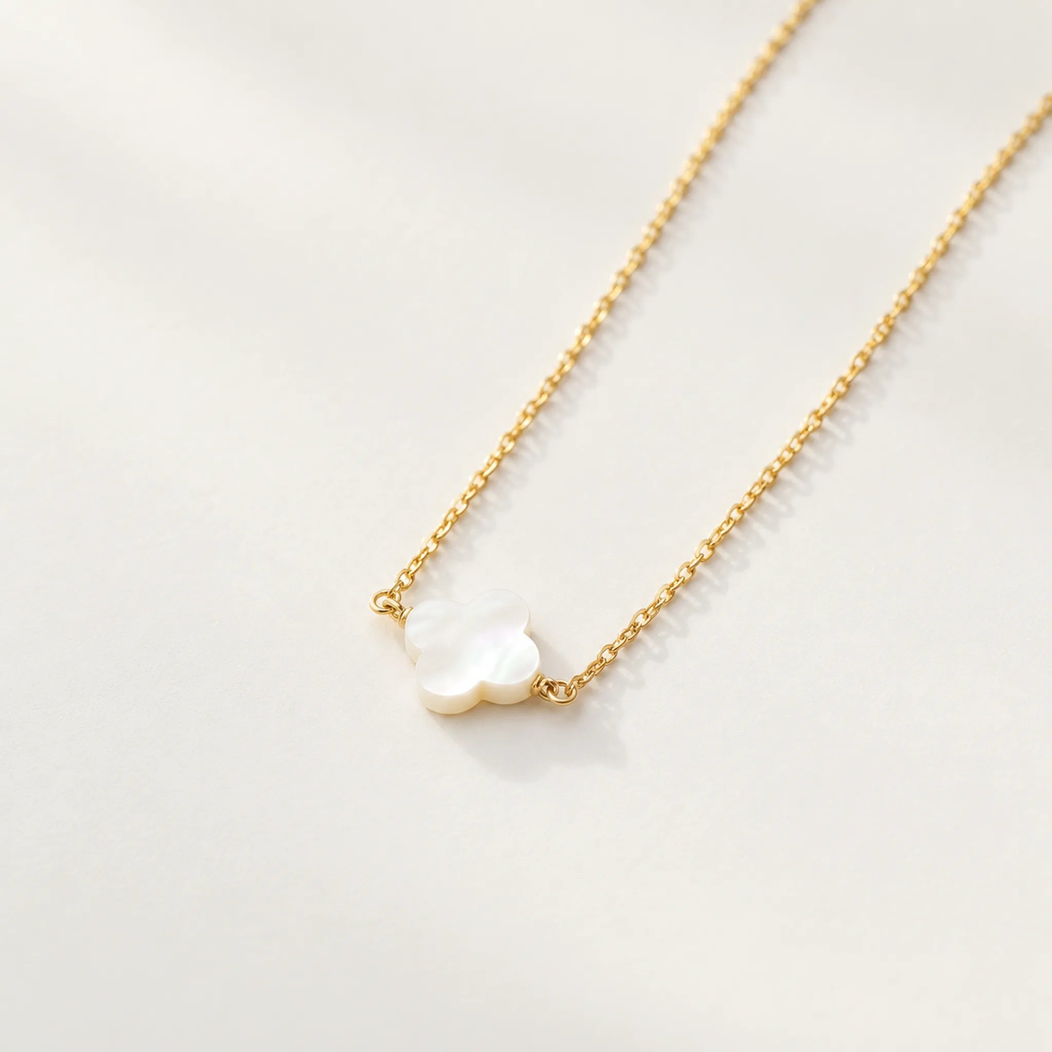 Gold mother of pearl clover necklace arranged diagonally on warm white