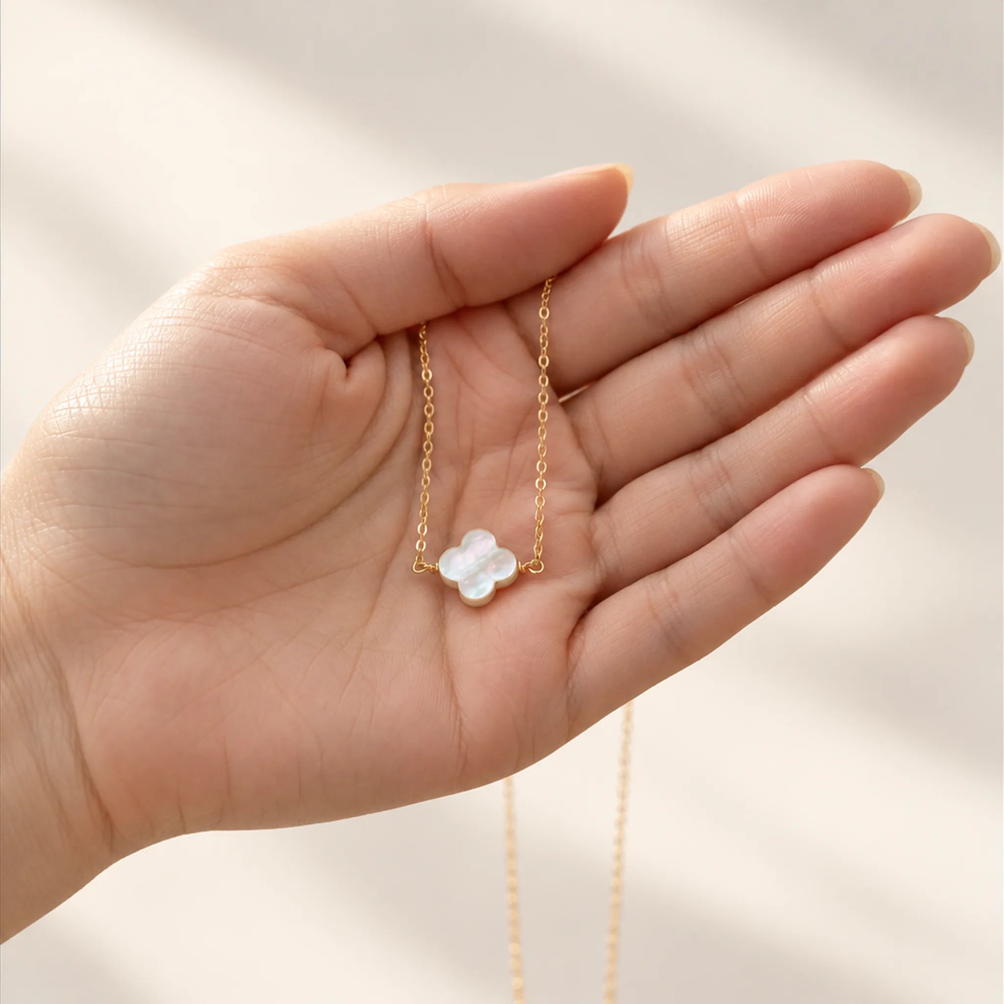 Gold mother of pearl clover necklace held in an open hand