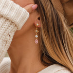 Woman wearing gold white topaz, sapphire and rose quartz drop earrings