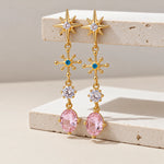 Gold gemstone drop earrings with pink stones on a beige surface