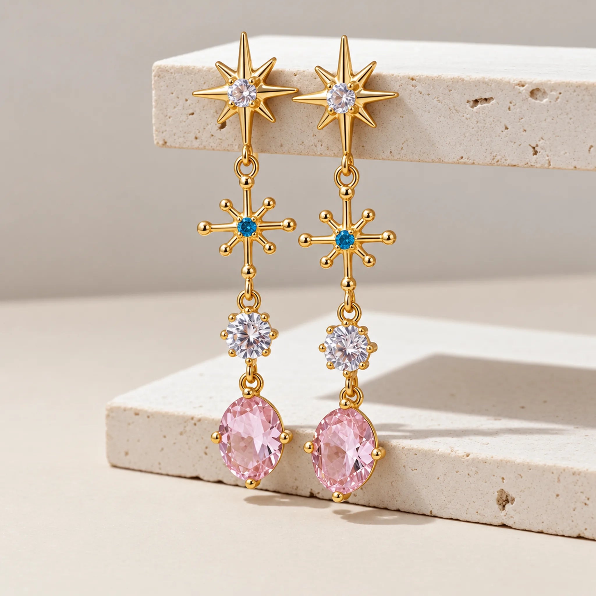 Gold gemstone drop earrings with pink stones on a beige surface