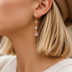 Close-up of a gold gemstone drop earring with pink rose quartz being worn