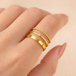 Gold stacker rings on a finger against a beige background
