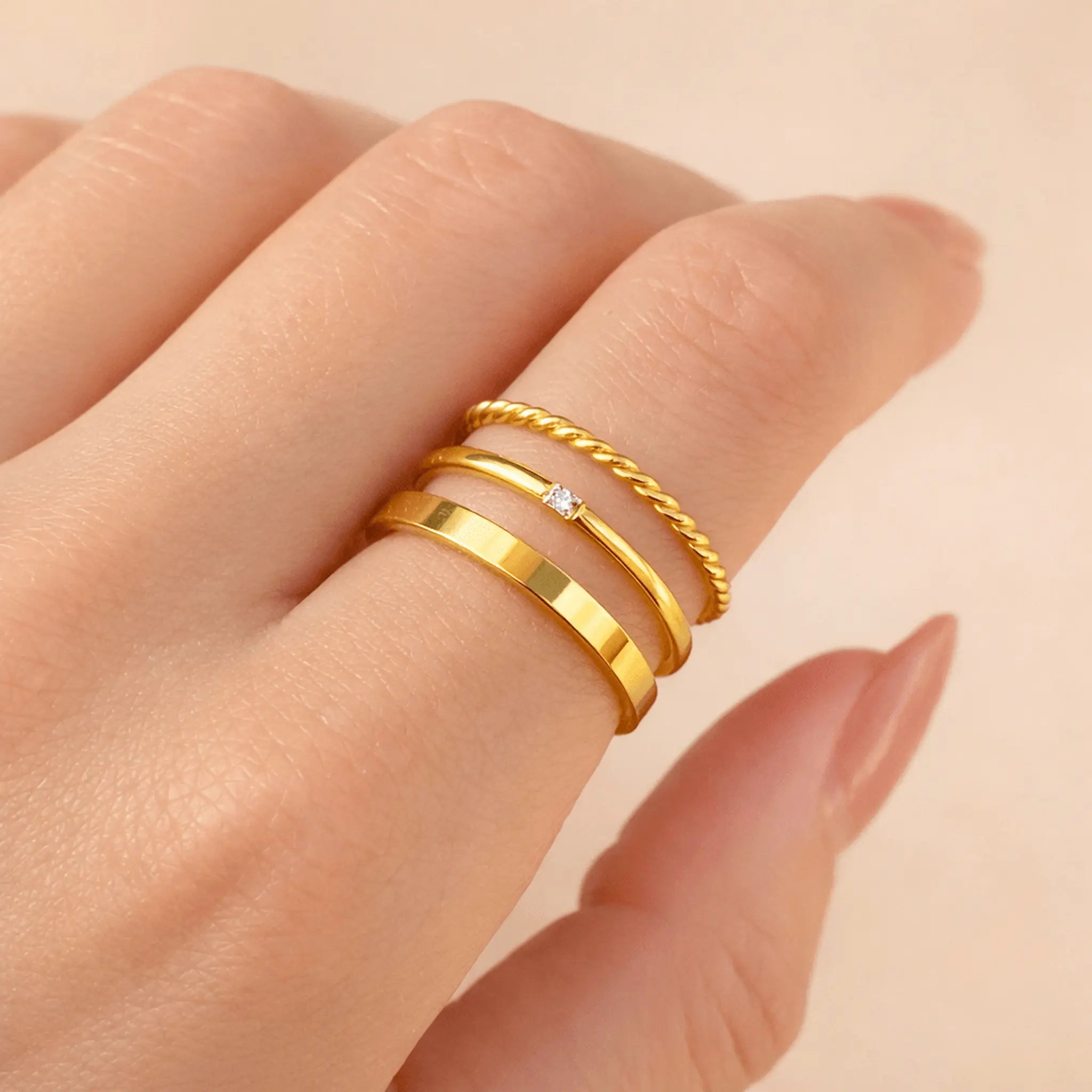 Gold stacker rings on a finger against a beige background