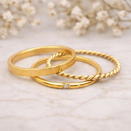 Three gold stacker rings on a marble surface with a soft floral background