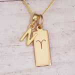 gold N initial and aries zodiac necklace on fine gold chain against a light wooden background