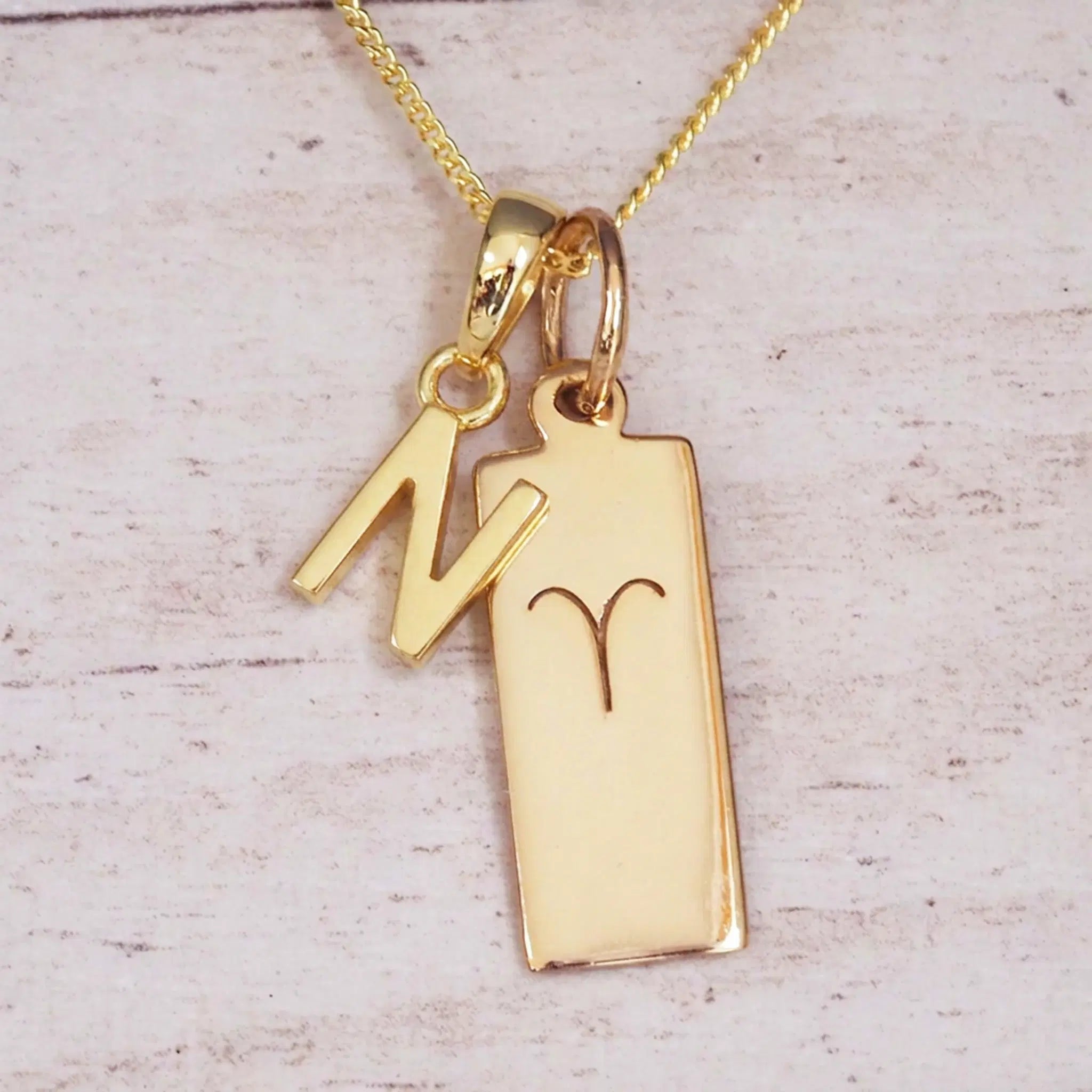 gold N initial and aries zodiac necklace on fine gold chain against a light wooden background