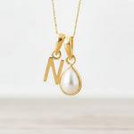 Gold necklace with a 'N' pendant and a teardrop-shaped pearl on a light background