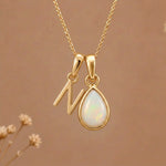Gold Initial N Pendant and October birthstone Natural Opal Necklace against a warm background