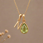 Gold Initial N Pendant and August birthstone Natural Peridot Necklace against a warm background