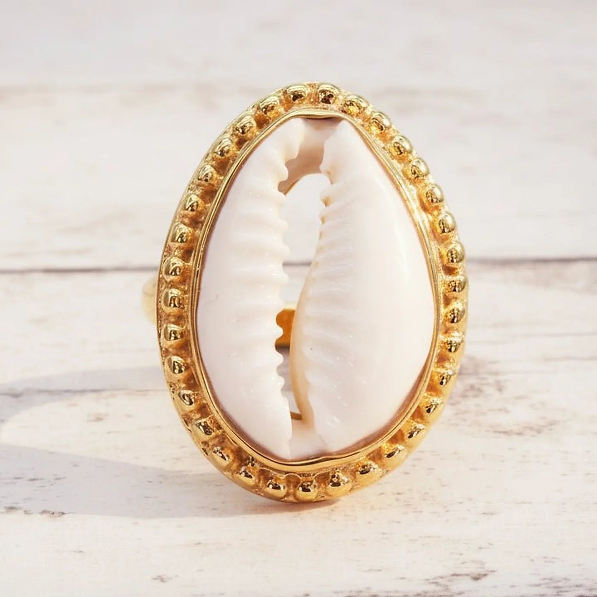 Gold cowrie shell ring on a light wooden surface
