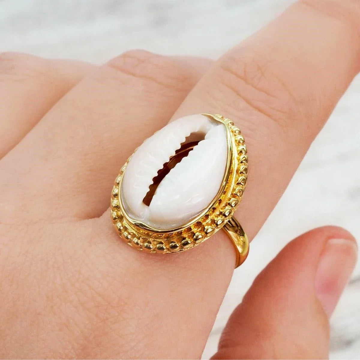 Gold cowrie shell ring worn on the finger