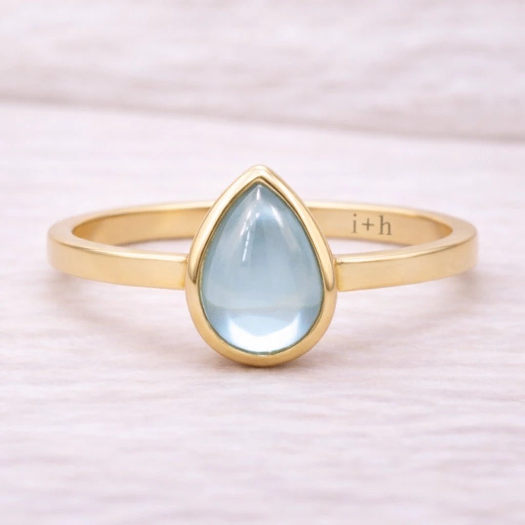 Gold ring with a teardrop-shaped light blue natural topaz gemstone on a white background