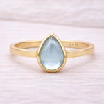 Gold ring with a teardrop-shaped light blue natural topaz gemstone on a white background