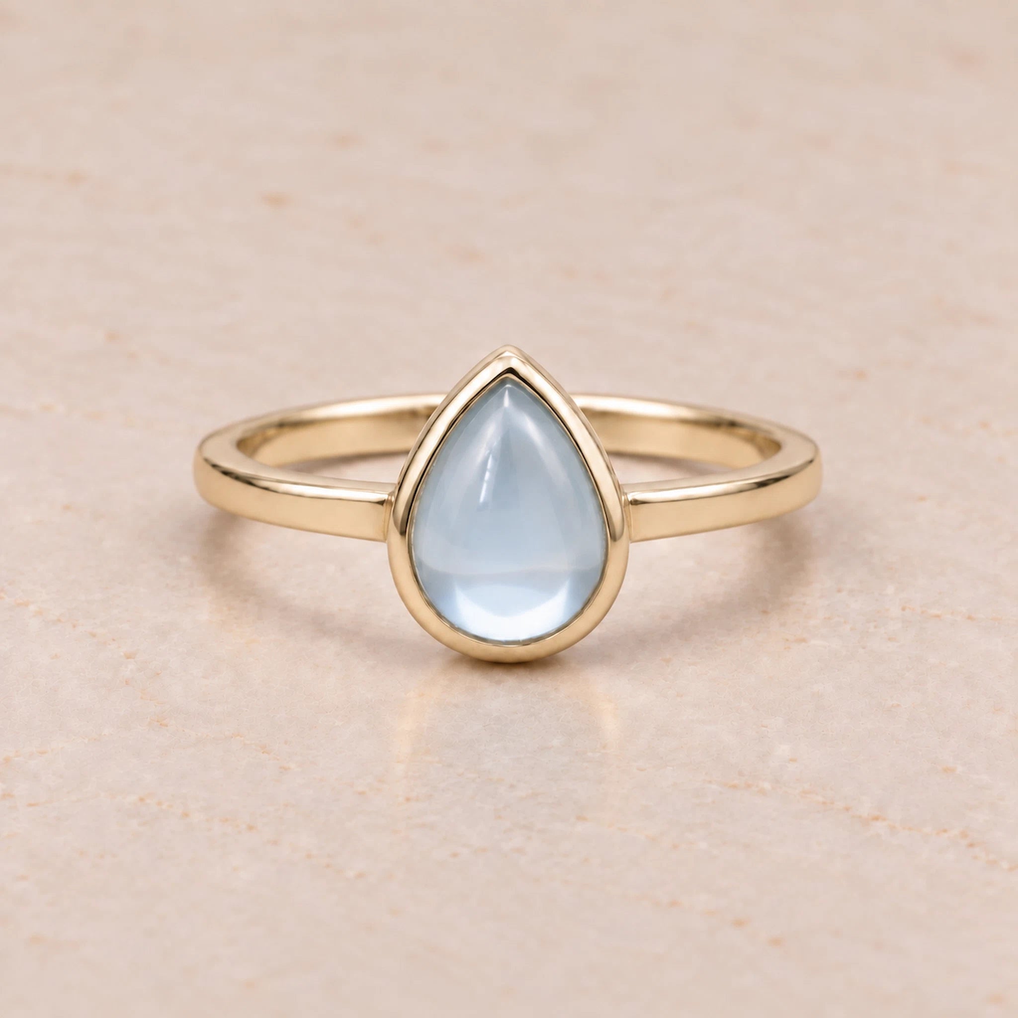 Gold November birthstone ring with a teardrop-shaped light blue natural topaz gemstone on a white background