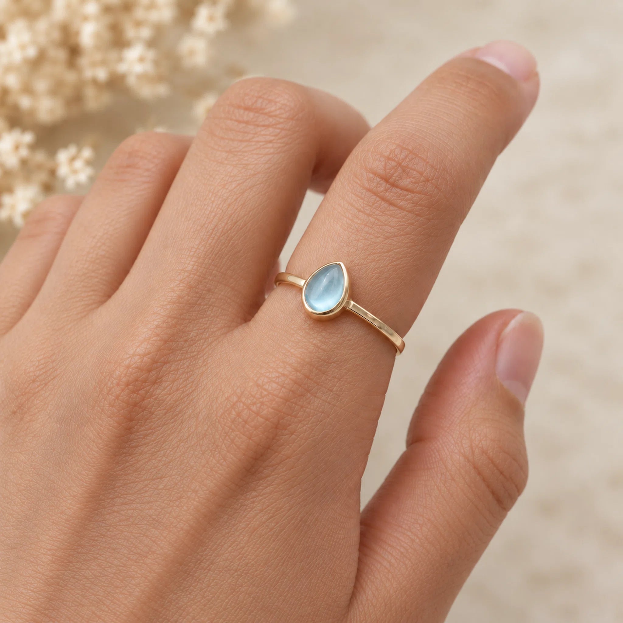 Gold ring with a light blue natural topaz gemstone on a person's finger against a white background