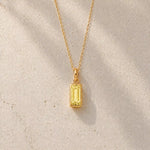 Gold fine chain necklace with a rectangle faceted bezel set november cubic zirconia pendant on a light stone background.