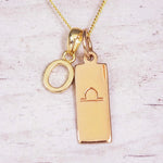 Gold initial and Libra zodiac necklace with a letter O charm and engraved bar pendant on whitewashed wood