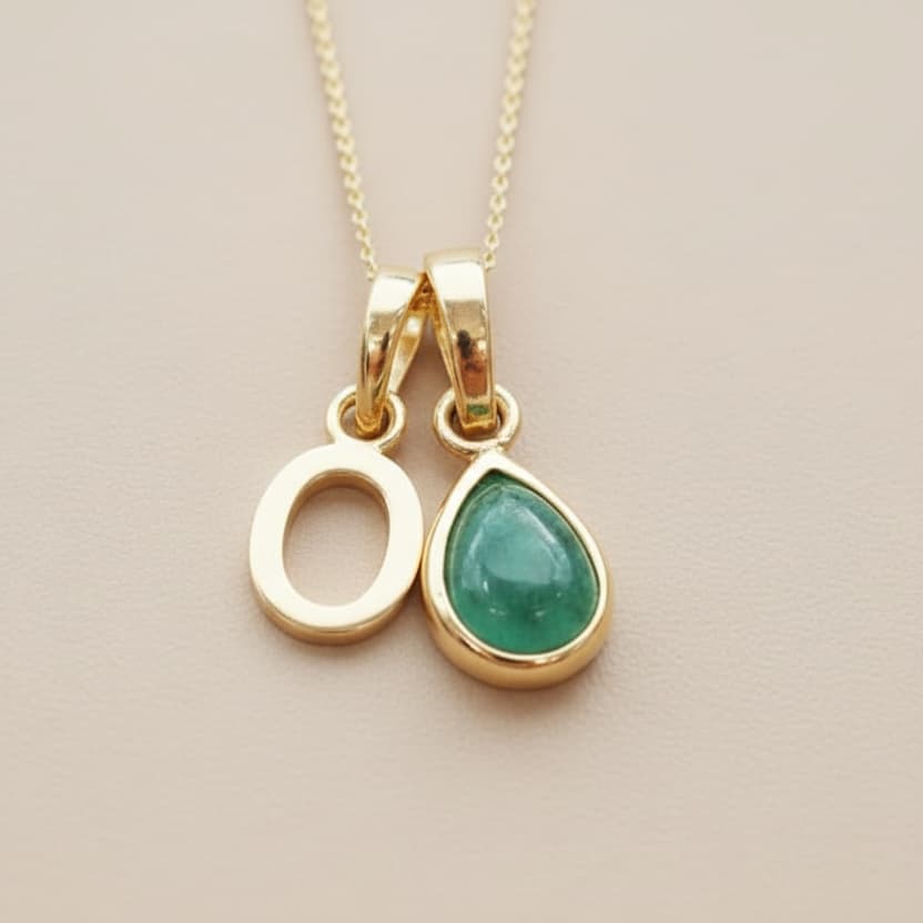 Two gold pendants with green gemstones on a beige background