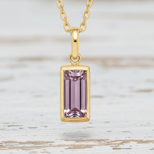 Gold necklace with a pink gemstone pendant on a white background